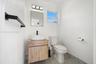 Wood-finish vanity cabinet, rectangular vessel sink, matte black wall-mounted faucet, framed wall mirror, and neutral tile flooring