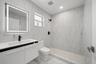 Bathroom featuring full-height stone-finish wall tile, walk-in shower with pebble-stone flooring, integrated LED vanity mirror, white cabinetry with a