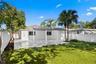 Rear exterior featuring a covered patio, paved tile flooring, enclosed white vinyl fencing, and palm trees