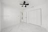 Interior room featuring white-veined large-format tile flooring, a matte black ceiling fan with integrated lighting, and white bi-fold closet doors