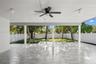 Covered patio featuring stone-finish flooring, a ceiling fan, dual overhead light fixtures, and a white vinyl privacy fence surrounding the rear groun