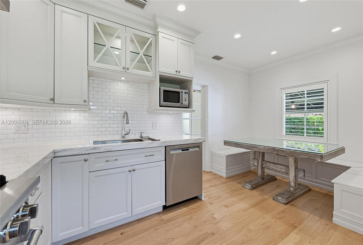 Kitchen featuring white shaker-style cabinetry, subway tile backsplash, stone-finish countertops, stainless steel appliances, and integrated bench sea