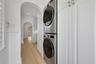 Stacked stainless steel laundry appliances, floor-to-ceiling cabinetry, wood-finish flooring, and arched architectural openings