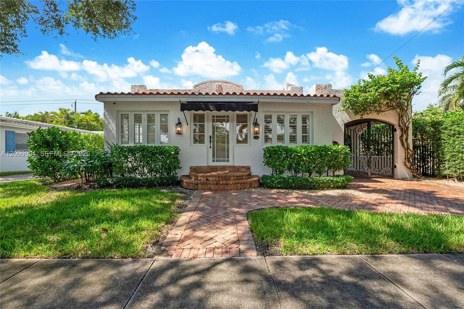 Spanish-style exterior featuring a clay tile roof, stucco facade, arched gate, brick paver walkway, and stone-tread entry steps