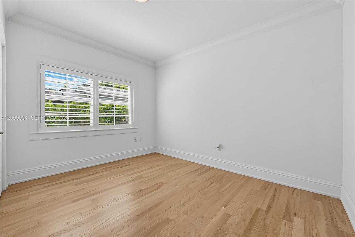 Interior space featuring wood-finish flooring, crisp white walls, crown molding, and plantation shutters