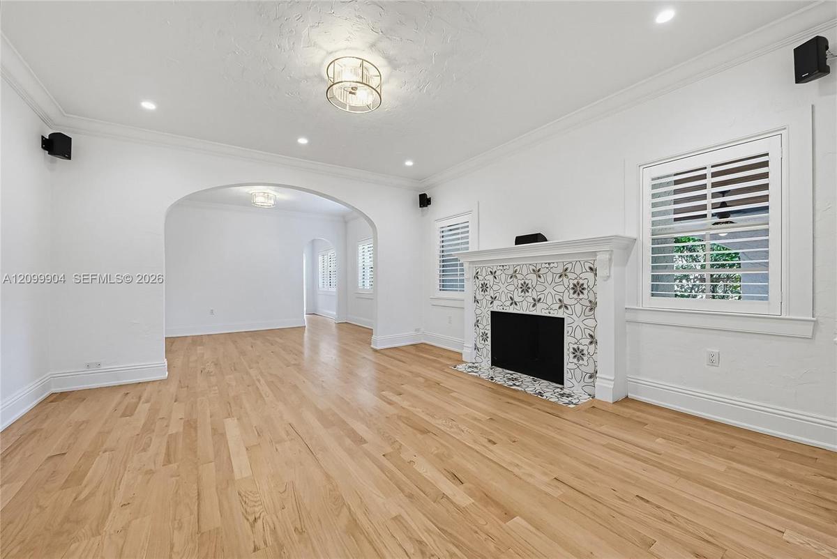 Living area featuring wood-finish flooring, a decorative tile-surround fireplace, arched architectural entryways, crown molding, and plantation shutte