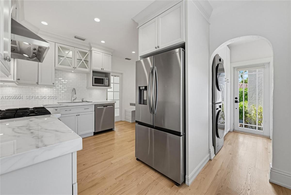 Kitchen featuring white shaker-style cabinetry, stone countertops, subway tile backsplash, stainless steel appliances, and wood-finish flooring