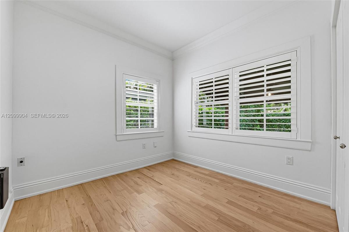Room featuring wood-finish flooring, white walls, crown molding, and windows fitted with white plantation shutters
