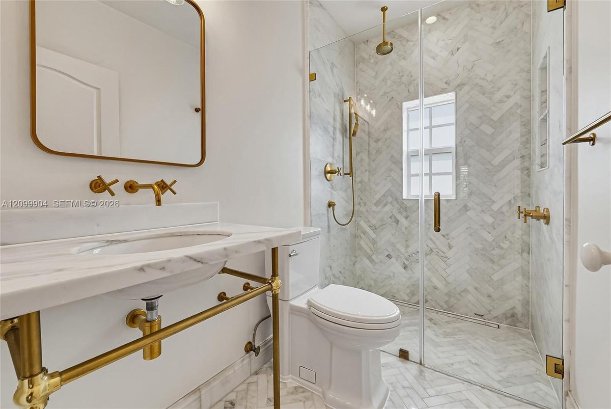 Wall-mounted brass faucets, marble-surround vanity with integrated sink, walk-in shower with herringbone tile, brass hardware, and glass shower enclos