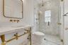 Wall-mounted brass faucets, marble-surround vanity with integrated sink, walk-in shower with herringbone tile, brass hardware, and glass shower enclos