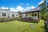 Rear exterior featuring a brick-paved patio, retractable scalloped awning, and stone-accented support columns, finished with a synthetic turf lawn and