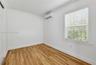 Wood-finish flooring, crown molding, wall-mounted ductless air conditioning unit, and a window with horizontal blinds