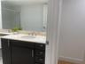 Kitchen featuring a waterfall-edge stone island, light-toned flat-panel cabinetry, stone backsplash, stainless steel range hood, and wood-finish floor