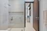 Walk-in shower featuring glass enclosure, wall-mounted rainfall showerhead, and integrated recessed shelving, complemented by a solid wood-finish door
