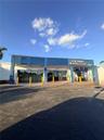 Commercial building exterior featuring blue metal paneling, floor-to-ceiling glass storefront windows, and an asphalt parking lot