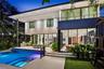 Contemporary two-story residence featuring expansive floor-to-ceiling glass sliding doors, a built-in outdoor kitchen, a private swimming pool with in