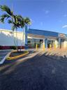 Commercial storefront exterior featuring expansive glass windows, paved asphalt parking, and a manicured palm tree planter
