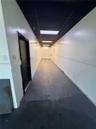 Hallway featuring smooth painted walls, high-contrast dark ceiling panels, recessed fluorescent lighting, and durable gray flooring