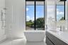 Freestanding soaking tub, floor-to-ceiling window, glass-enclosed shower with rainfall showerhead, and dual-drawer vanity with white countertop