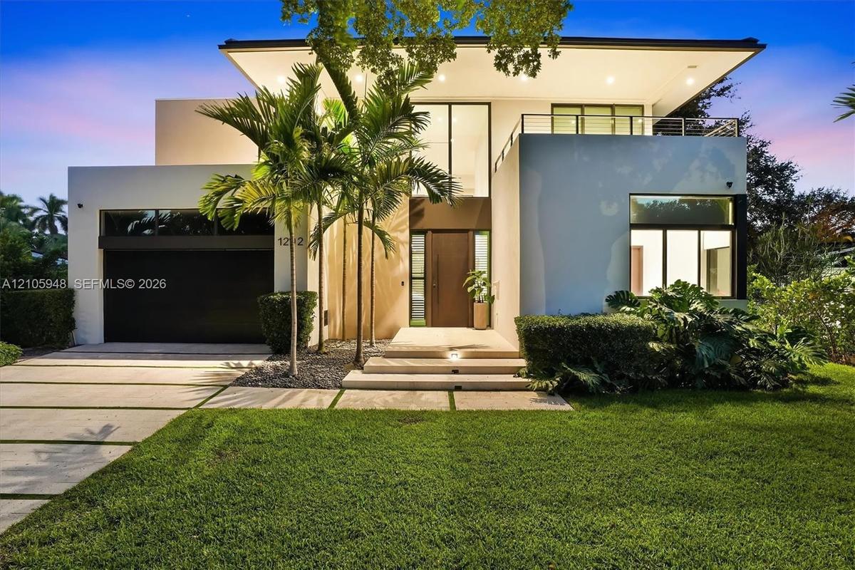 Contemporary architectural exterior featuring a stucco facade, second-story balcony with metal railing, oversized glass entryway, and a concrete paver