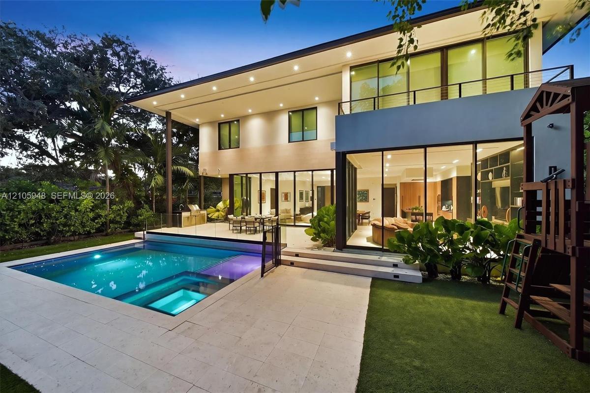 Modern residence featuring floor-to-ceiling glass sliding doors, a two-story balcony with metal railings, a paved stone pool deck, and a recessed swim
