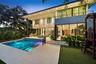 Modern residence featuring floor-to-ceiling glass sliding doors, a two-story balcony with metal railings, a paved stone pool deck, and a recessed swim