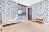 Room featuring floral patterned wallpaper, light wood-finish flooring, a black-framed window, and a dark wood-finish interior door with recessed ceili