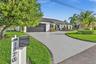 Single-story residence featuring a tile roof, light-toned exterior finish, multi-car garage, expansive concrete driveway, and established landscaping