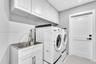 Laundry room featuring white shaker-style upper and lower cabinetry, an integrated stainless steel utility sink with a high-arch pull-down faucet, dar