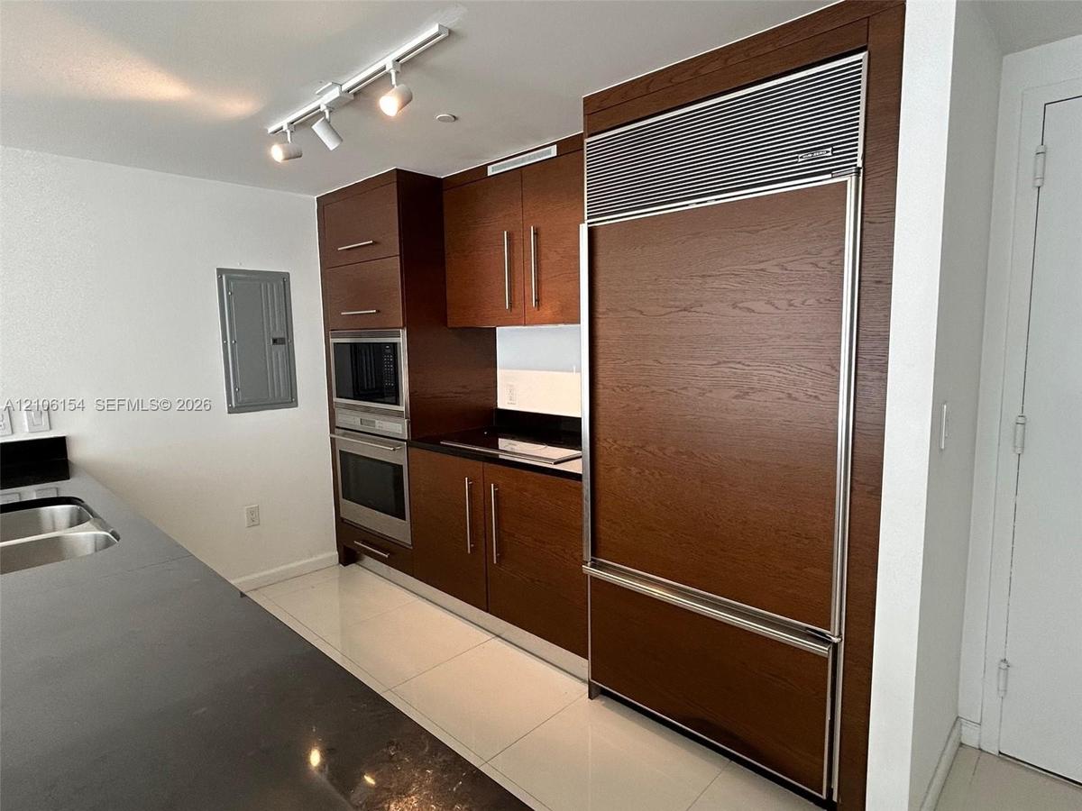 Kitchen featuring custom wood-finish cabinetry, integrated panel-ready refrigerator, stainless steel built-in wall oven and microwave, dark stone coun