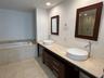 Double vanity featuring a light-toned stone countertop, dual vessel sinks, dark wood-finish cabinetry, and a deep soaking tub with a stone tile surrou