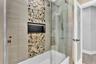 Shower and tub combination featuring horizontal tile surrounds, a decorative vertical pebble-tile inlay, integrated black-framed shower niche, glass s