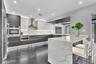 Kitchen featuring two-tone flat-panel cabinetry, a waterfall-edge stone countertop, integrated stainless steel appliances, and under-cabinet accent li