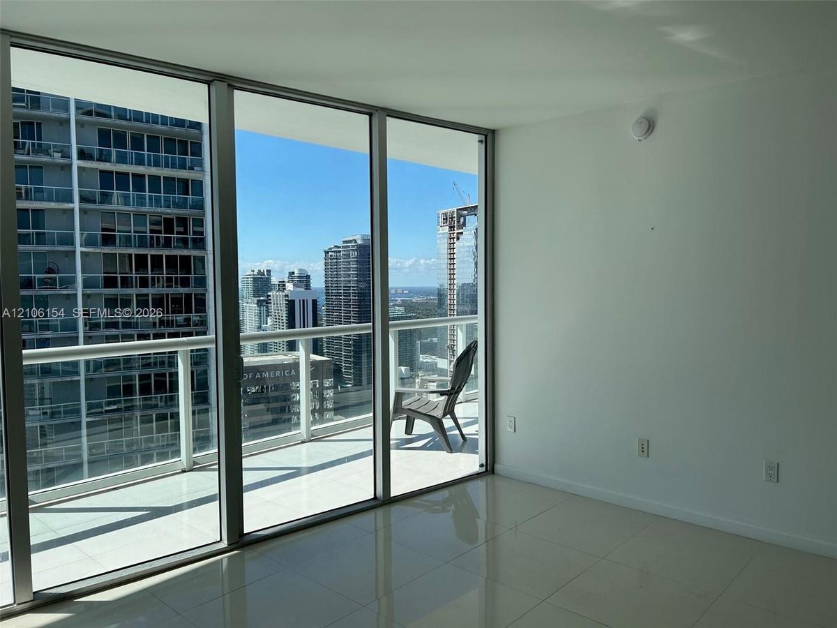 Floor-to-ceiling glass walls, polished tile flooring, and a private balcony with metal railings and a glass surround