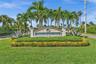Palm Beach Isles community entrance featuring a stone monument sign, manicured lawn, established palm trees, and structural landscape hedging