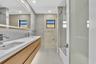 Floating double vanity with a stone countertop and dual undermount sinks, illuminated mirror, wood-finish cabinetry, and a glass-enclosed shower featu