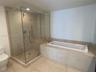 Walk-in glass-enclosed shower with integrated seating, drop-in soaking tub with stone tile surround, and neutral stone tile flooring