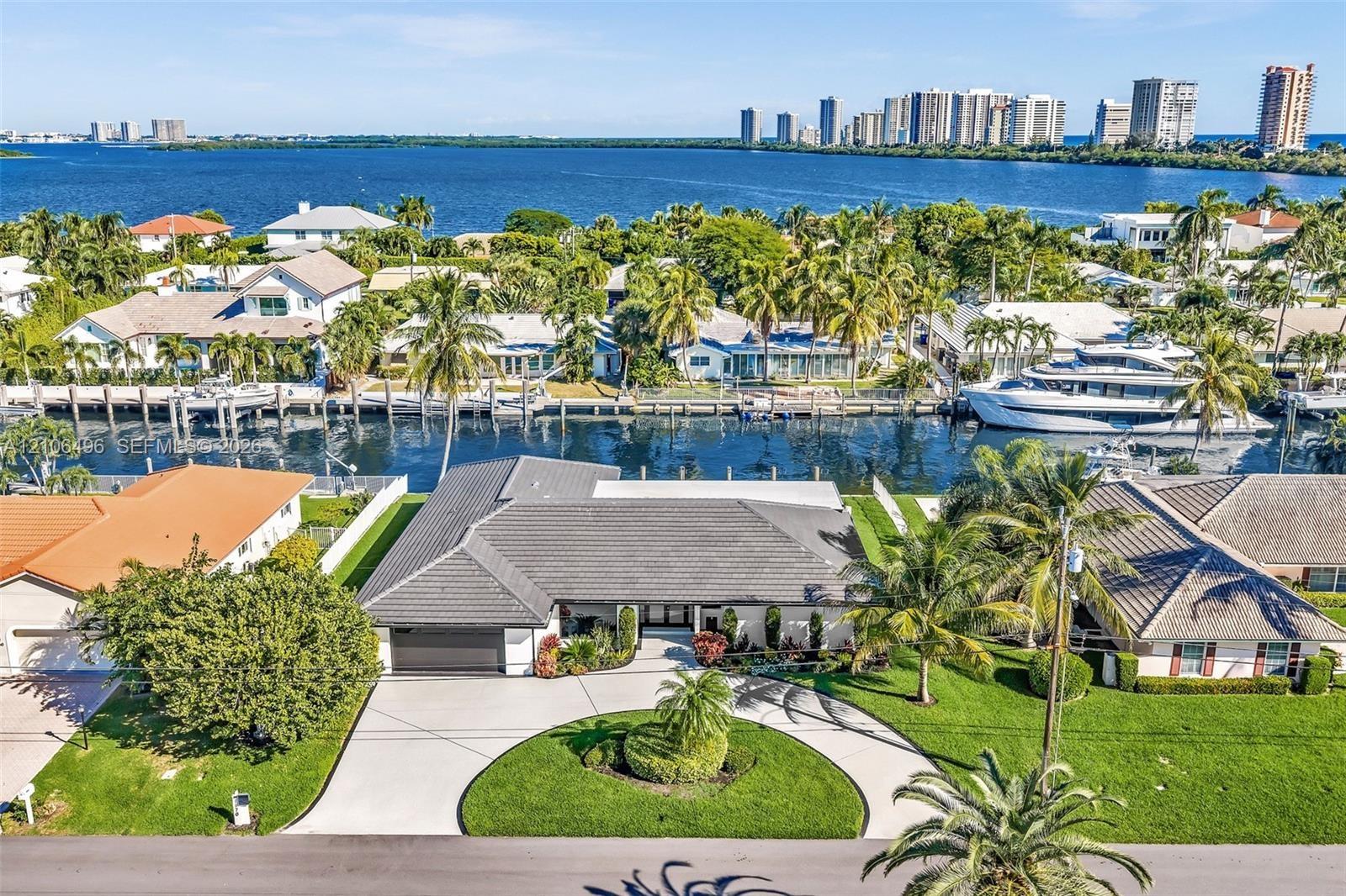 Waterfront single-story residence featuring a tile roof, concrete circular driveway, manicured lawn, and mature palm trees