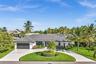 Single-story residence featuring a low-pitched tiled roof, a circular concrete driveway, and an attached two-car garage, complemented by mature tropic