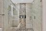 Walk-in shower featuring large-format neutral wall tile, a vertical pebble-stone accent column, pebble-tile flooring, a recessed storage niche, and an