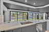 Large kitchen island with white countertop, undermount stainless steel sink, gooseneck faucet, gray flat-panel cabinetry, and extensive sliding glass 