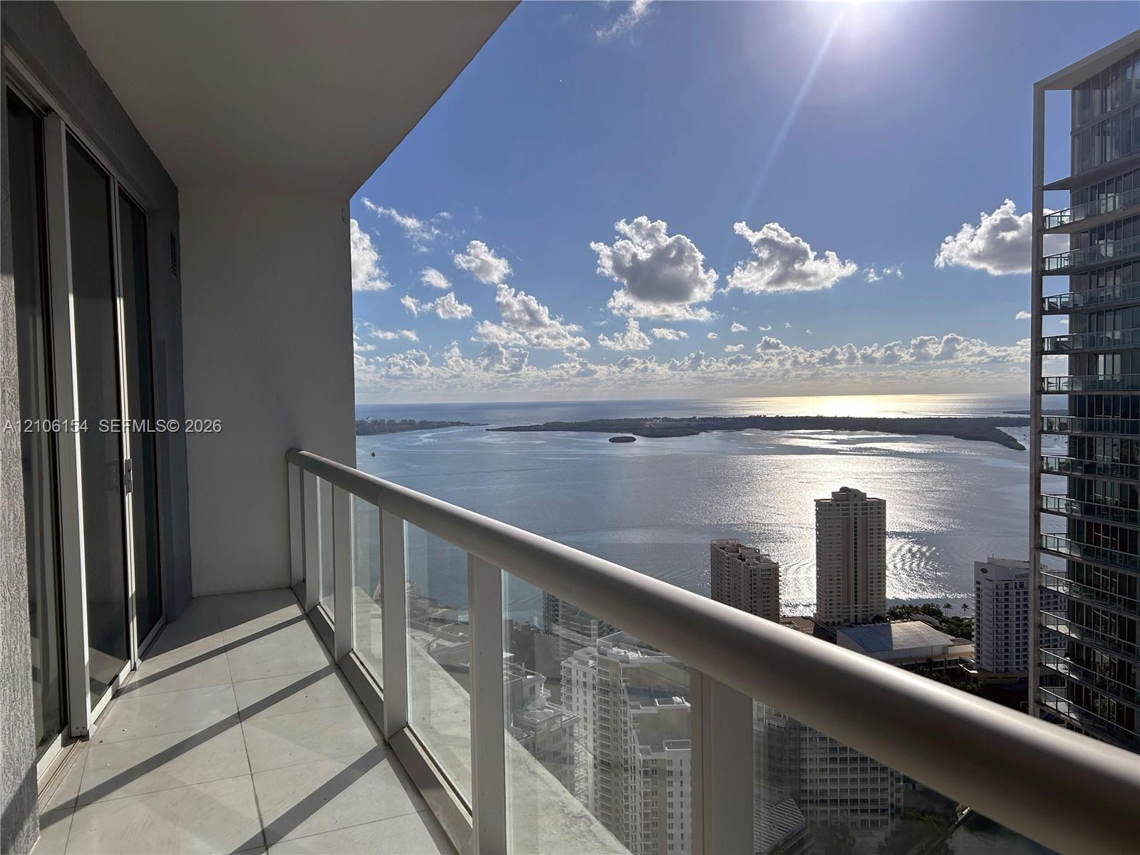 Private covered balcony with tile flooring and a glass panel railing