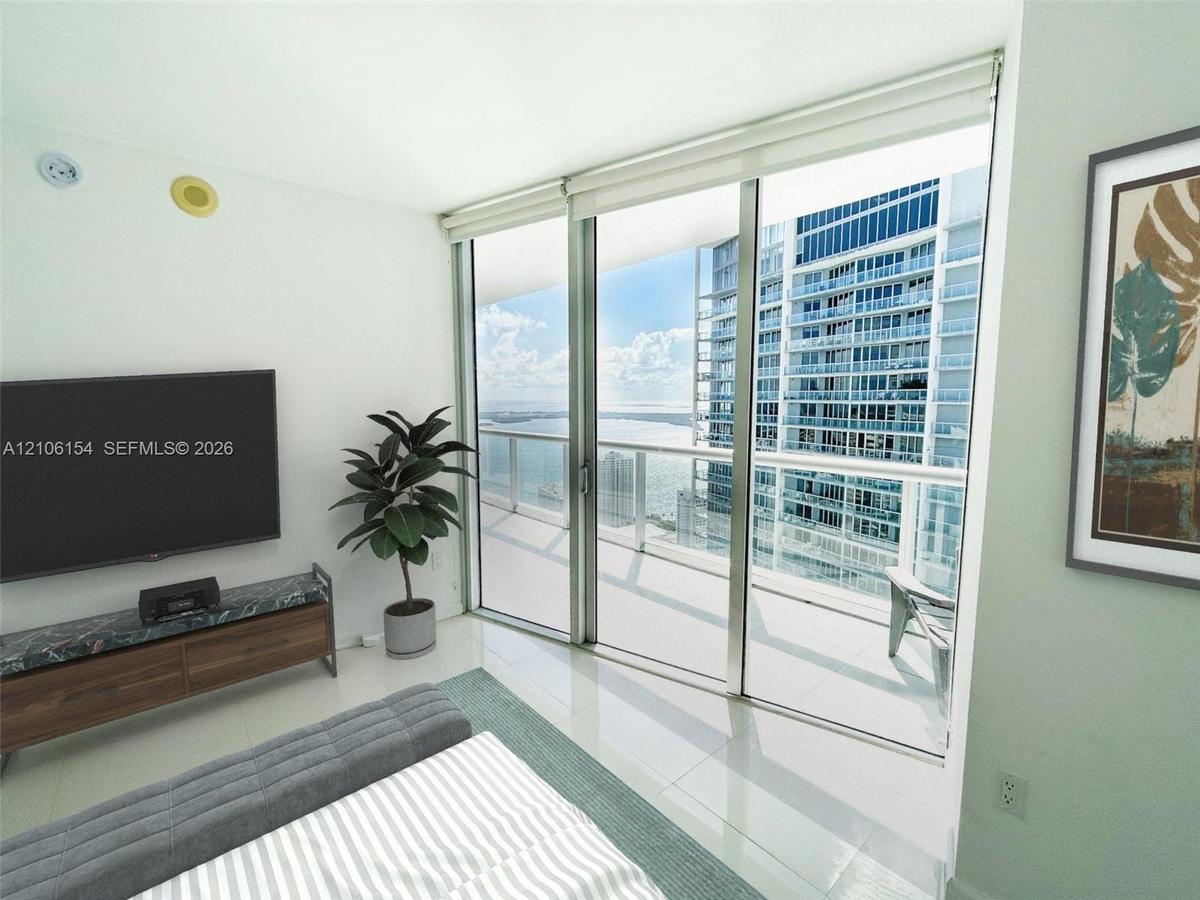 Floor-to-ceiling glass sliding doors opening to an expansive balcony, polished tile flooring, and integrated motorized window shades