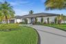 Single-story residence featuring a low-pitched tiled roof, smooth stucco exterior, circular concrete driveway with decorative border, and established 