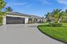 Single-story exterior featuring white stucco siding, a multi-car garage with overhead glass-paneled door, a curved concrete driveway, and mature lands