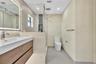 Floating wood-finish vanity with an integrated rectangular sink, backlit vanity mirror, glass-enclosed shower with decorative stone-look inlay, and la