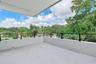 Covered balcony featuring neutral stone tile flooring, a solid half-wall enclosure, and a black metal railing