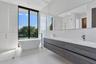 Modern bathroom featuring a freestanding soaking tub, dual-sink wall-mounted vanity with dark wood-finish cabinetry, white solid-surface countertop, f