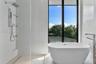 Freestanding soaking tub with floor-mounted faucet, walk-in shower with large-format tile surround, rainfall showerhead, and integrated glass shelving