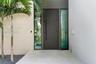 Entry featuring a dark horizontal-plank door with an elongated vertical handle, framed by full-height frosted glass sidelights on a neutral-toned ston